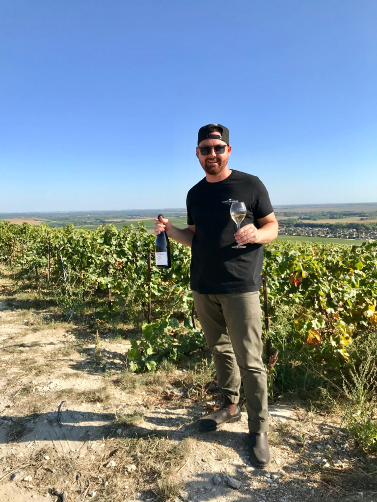 Sommelier Daniel McDonough holding champagne in a vineyard in Champagne, France