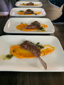 Lamb chop on squash puree with herb oil, plated on a white rectangular plate
